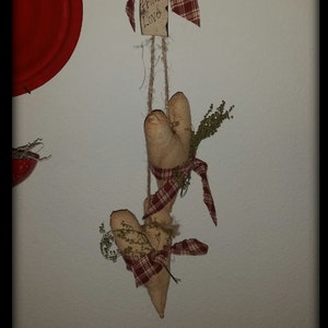 May include: Two rustic fabric hearts with red and white plaid ribbon hanging from a twine string with a small tag that reads "Prim Love".