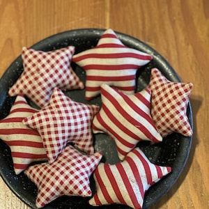 May include: A collection of seven red and white fabric stars in a black metal bowl. The stars are made of gingham and striped fabric.