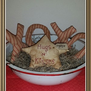 May include: A white ceramic bowl with a red rim filled with brown dried moss and three red and white striped fabric letters spelling "XOX" and a star-shaped fabric piece with the text "Hugs 'n Kisses" and a small tag with the text "XOXO".