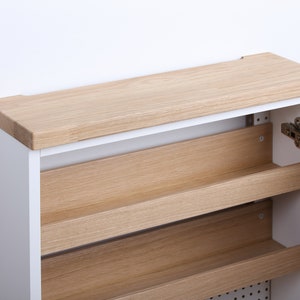 May include: White shoe cabinet with a wooden top and shelves. The cabinet door is open, revealing the interior shelves.