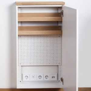 May include: A white cabinet with a wood top and a pegboard door. The door is open and reveals a row of electrical sockets and two shelves.