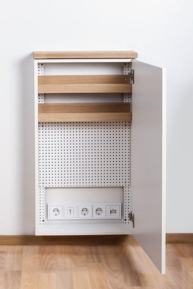 May include: A white cabinet with a wood top and a pegboard door. The door is open and reveals a row of electrical sockets and two shelves.