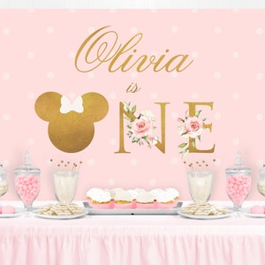 Puede incluir: Tel&oacute;n de fondo de fiesta rosa y dorado con lunares blancos. El tel&oacute;n de fondo presenta una cabeza de Mickey Mouse dorada con un lazo rosa, el nombre "Olivia" en escritura dorada y las palabras "is one" en letras doradas con acentos florales rosas.