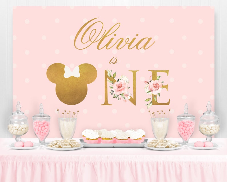 Puede incluir: Tel&oacute;n de fondo de fiesta rosa y dorado con lunares blancos. El tel&oacute;n de fondo presenta una cabeza de Mickey Mouse dorada con un lazo rosa, el nombre "Olivia" en escritura dorada y las palabras "is one" en letras doradas con acentos florales rosas.
