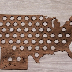 May include: A wooden map of the United States with 50 circular cutouts for bottle caps. The map is stained a dark brown color.