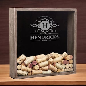 May include: A wooden box with a glass front filled with wine corks. The box has a black background with a white logo that says "Hendricks Winery Est. 2007" with a monogram of the letter "H" in a circle.