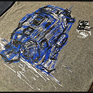 May include: A gray t-shirt with a blue and black sketch of a robot on the front. The robot is drawn in a stylized, graffiti-like style. The text "RED" is written in white on the right side of the shirt.