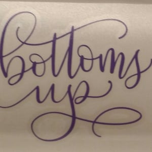 May include: Purple vinyl decal with the words "bottoms up" written in a cursive font.