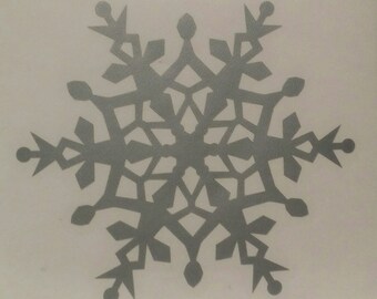 May include: A silver snowflake sticker with a detailed, intricate design. The snowflake is symmetrical and has a six-pointed star shape.
