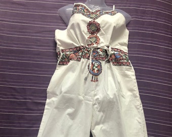 May include: White cotton jumpsuit with a colorful floral print and a drawstring waist. The jumpsuit has a wide leg and a sleeveless design.