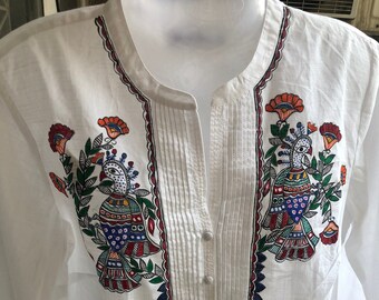 May include: White cotton tunic top with a V-neck and long sleeves. The top features a hand-painted design of peacocks and flowers in shades of red, blue, green, and orange.