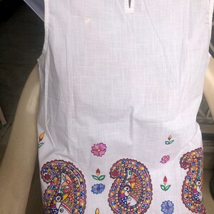May include: White sleeveless top with a paisley pattern in shades of red, blue, yellow, and green. The paisley pattern features stylized fish and floral motifs. The top has a button closure at the back of the neck.