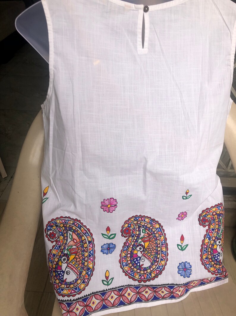 May include: White sleeveless top with a paisley pattern in shades of red, blue, yellow, and green. The paisley pattern features stylized fish and floral motifs. The top has a button closure at the back of the neck.