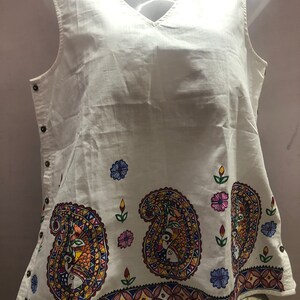 May include: White sleeveless top with a V-neck and a colorful paisley design on the bottom hem.