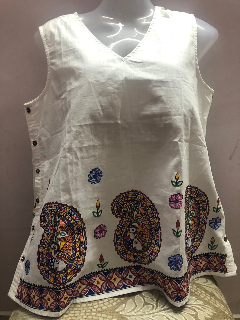 May include: White sleeveless top with a V-neck and a colorful paisley design on the bottom hem.