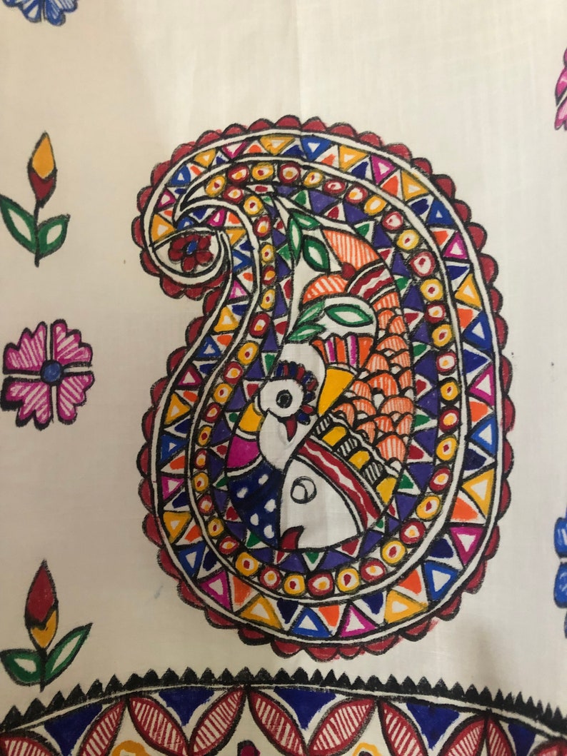 May include: A white fabric with a colorful paisley design. The paisley is filled with geometric shapes and a peacock design. The fabric is decorated with other floral designs.