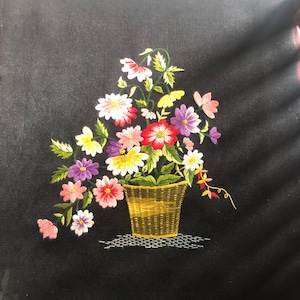 Può includere: Ricamo floreale su uno sfondo di tessuto nero. Il disegno presenta un bouquet di fiori rosa, bianchi, gialli, viola e rossi in un cesto intrecciato marrone.