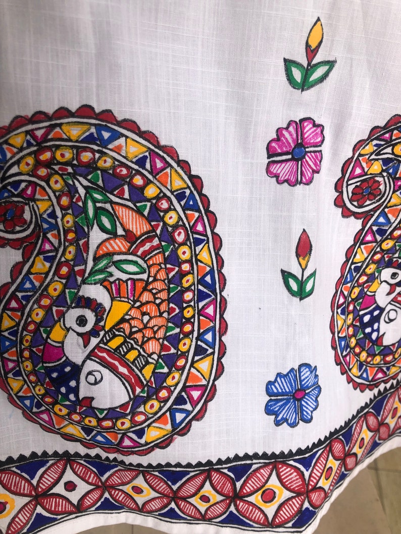 May include: White fabric with a colorful paisley design. The paisley is outlined in red and filled with a variety of colors, including blue, yellow, orange, and green. The fabric also features a border of red, yellow, and blue.