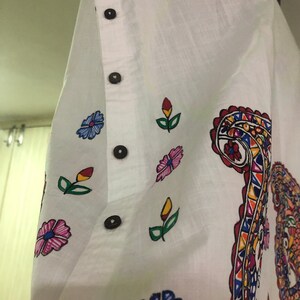 May include: White cotton shirt with a colorful paisley design and floral accents. The shirt has a button-up closure and a relaxed fit.
