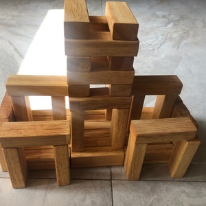 Könnte beinhalten: Ein Holzblock-Turmbausatz mit mehreren Teilen, die zu einer hohen Struktur mit Bögen und Öffnungen gestapelt werden. Die Blöcke sind aus Naturholz und haben eine hellbraune Farbe.