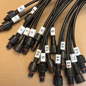 May include: A close-up of 15 black electrical connectors with red rubber seals. Each connector is labeled with a white sticker with a number from 1 to 15.