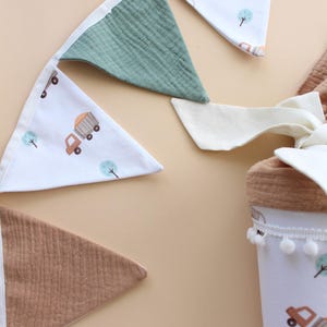 May include: A collection of nursery decor featuring a banner and a container. The banner has alternating triangle flags in white with truck and tree illustrations, green, and brown. The container is white with a truck and tree pattern and a pom-pom trim.