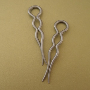 May include: Two silver hair clips with a wavy design. The clips are made of metal and have a shiny finish.