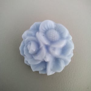 May include: A pale blue, flower-shaped decorative object. The object is a cluster of sculpted flowers, with petals and a central flower design. The object is likely made of glass or a similar material.