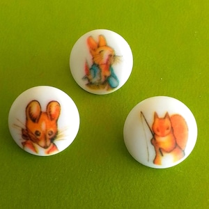May include: Three white round buttons with different illustrations of children's book characters. The first button features a rabbit wearing a blue jacket, the second button features a mouse wearing a red jacket, and the third button features a squirrel wearing a brown jacket.
