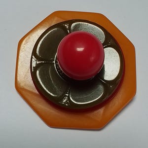 May include: A multi-layered, octagonal, orange, brown, and red button with a flower design.