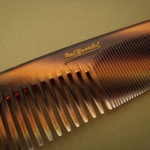 Könnte beinhalten: Ein Kamm mit Schildpattmuster und dem goldenen Text "Paul Marcel". Der Kamm hat eng stehende Zähne und ein gebogenes Design. Ein Haarpflege-Accessoire.