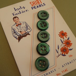 May include: A set of five round, dark green buttons with four holes, attached to a white display card. The card features the text Lady Fashion SHIRT PEARLS, an illustration of a person in a shirt, a floral graphic, and the text 10c ATTRACTIVE No. 114C.