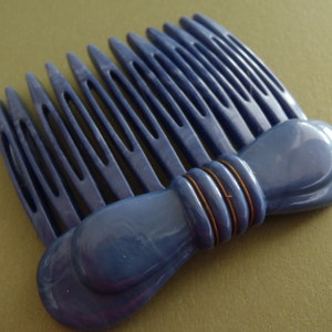 May include: A blue plastic hair comb with a bow design. The comb has a row of teeth and a decorative bow on the bottom.