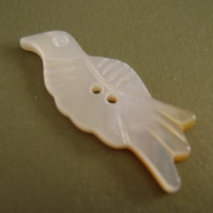 May include: A white mother of pearl button shaped like a bird with two holes for sewing.