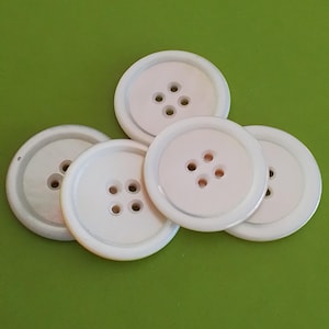 May include: Five white pearl buttons with four holes each. The buttons are arranged in a semi-circle on a green surface.