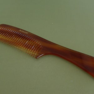 May include: A brown comb with a curved handle and fine teeth. The comb has a tortoiseshell pattern and is made of a translucent material. The comb is designed for hair grooming and styling.