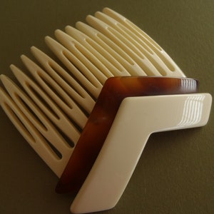 May include: A collection of vintage hair combs in cream, tortoiseshell, and white. The combs are arranged in a layered, fan-like design, showcasing their unique shapes and colors. The image highlights the classic design of the hair accessories.