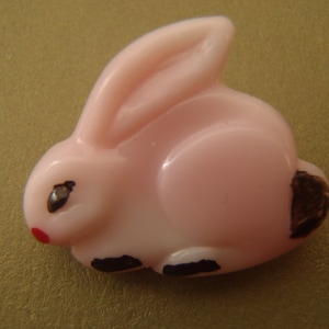 May include: A pink plastic button shaped like a rabbit with black eyes and a red nose.