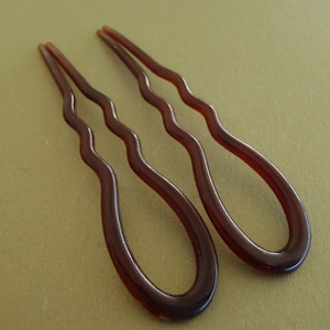 May include: Two brown plastic hair combs with a wavy design. The combs are approximately 12.5 cm long and have a rounded end.