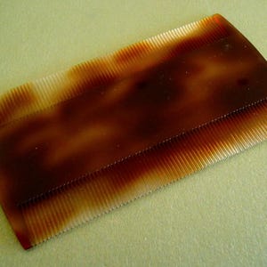 May include: A brown tortoiseshell comb with fine teeth. The comb is made of plastic and has a smooth, glossy finish.