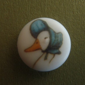 Könnte beinhalten: Ein weißer Keramikknopf mit einer blauen und weißen Illustration eines Entchens mit einem blauen Häubchen.