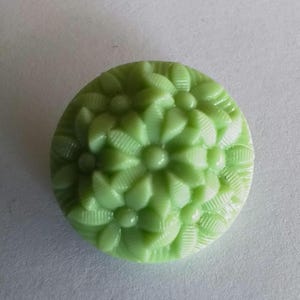 May include: A light green glass button with a raised floral design. The button has a smooth, shiny finish.