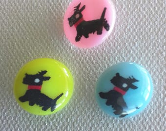 Può includere: Tre bottoni rotondi con silhouette nere di cani su di essi. I bottoni sono rosa, giallo e blu.