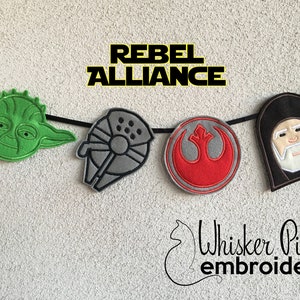 May include: A banner with the text "Rebel Alliance" and embroidered images of Star Wars characters, including Yoda, a TIE fighter, the Rebel Alliance symbol, and a hooded figure with a white beard.