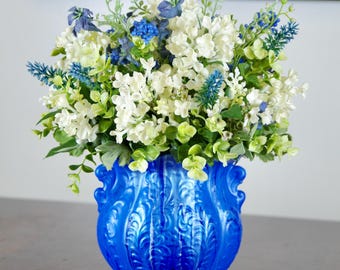 Arreglo floral de hortensias de seda azules, flores silvestres y bayas en un jarrón de cerámica pintado de azul.