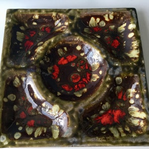 May include: A square ceramic serving dish with four sections. The dish has a brown, green, and red glaze with a speckled pattern. The centre section is larger and has a raised rim.