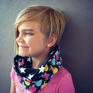 Puede incluir: Una persona joven con el pelo corto y rubio que lleva una camisa rosa y una bufanda negra y blanca con diseños de conos de helado de colores.