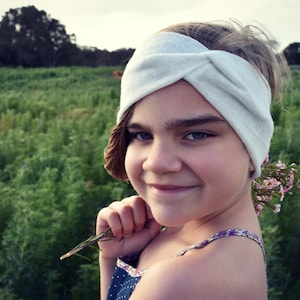 Puede incluir: Una persona joven con cabello castaño claro que lleva una diadema blanca anudada y un vestido estampado en azul y blanco. La persona sostiene un pequeño ramo de flores rosas.