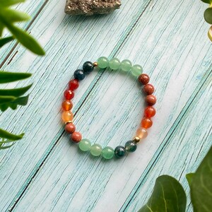 Peut inclure: Un bracelet en perles multicolores avec des perles vertes, brunes, orange et rouges. Le bracelet est fait de pierres naturelles et a un accent doré.