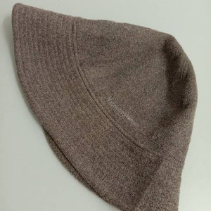 May include: A brown bucket hat made of a textured fabric. The hat has a wide brim and a simple design.